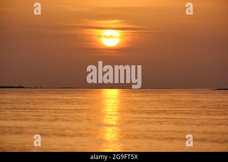 Große gelbe Sonne untergeht über der Meeresoberfläche. Stockfoto