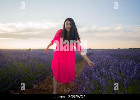 Junge glückliche und schöne asiatische japanische Frau im Sommerkleid genießen Natur frei und verspielt im Freien auf lila Lavendel Blumen Feld in romantischen Stockfoto