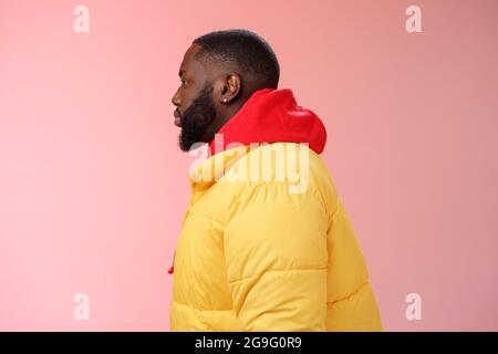 Profil Studio erschossen bärtigen jungen 25s afrikanischen Kerl in gelb Jacke rot Kapuzenpullover Look links normal unbeschwert entspannten Ausdruck stehen Warteschlangenreihenfolge Stockfoto