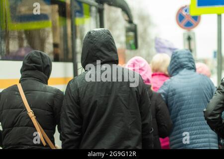 Menschen von hinten im Regen. Kapuzen gehen in Richtung Bus. Draußen regnet es. Schlechtes Wetter für die Menschen. Stockfoto