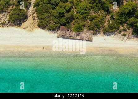 Luftaufnahme einer Person, die am leeren Gidaki-Strand in Ithaca am Berg und in der Nähe eines verlassenen Sommerkiosks läuft Stockfoto