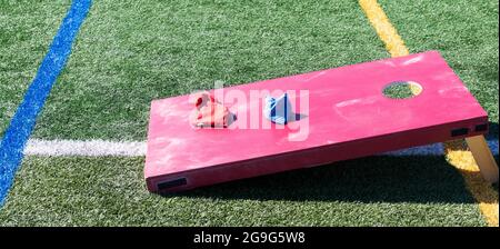 Eine rote selbstgemachte Kornloch-Bohnentasche wirft Spiel auf einem grünen Rasenfeld mit roten und blauen Tüten auf der Oberseite. Stockfoto