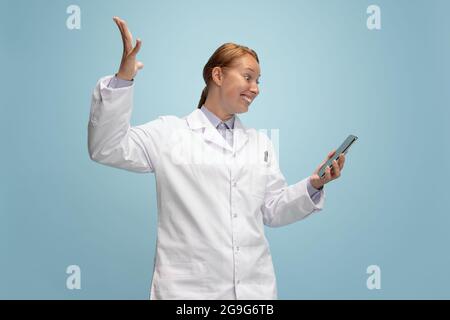 Porträt einer Ärztin, therapeutischen oder medizinischen Fachberaterin mit einem isolierten Smartphone-Bildschirm auf blauem Hintergrund. Lustige glückliche Emotionen. Konzept von Stockfoto