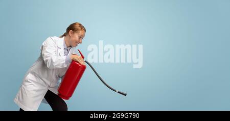 Porträt einer jungen Frau, eines Arztes, eines therapeutischen oder medizinischen Beraters mit einem auf blauem Hintergrund isolierten Feuerlöscher. Lustige Meme Emotionen. Stockfoto