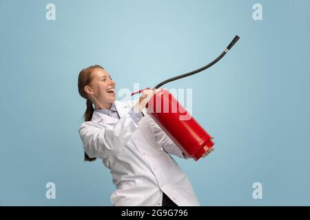 Porträt einer jungen Frau, eines Arztes, eines therapeutischen oder medizinischen Beraters mit einem auf blauem Hintergrund isolierten Feuerlöscher. Lustige Meme Emotionen. Stockfoto