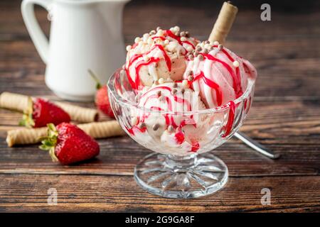Erdbeer-, Banane- und Rahm-Roma-Eis in einer Glasschüssel mit roter Sauce darüber gegossen. Stockfoto