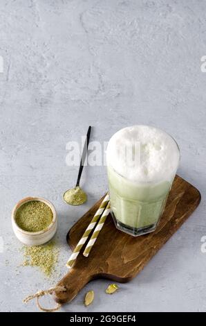 Matcha Grüner Tee, Kaffee Latte mit Schaumstoff in einer hohen Glasansicht von oben auf einem Holzbrett und einem betongrauen Hintergrund mit Kopierraum Stockfoto