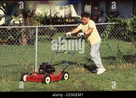 Austin, Texas USA,1988: Hispanischer Junge, 13, Rasenmähen mit gasbetriebenem Mäher. MR RR-0092. ©Bob Daemmrich Stockfoto