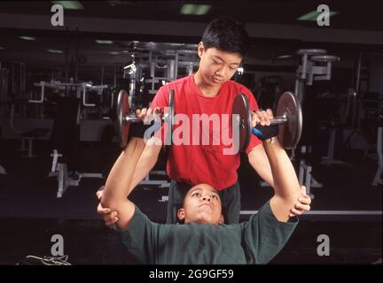 Austin, Texas USA, 1990: Übung: Schwarze und asiatische Teenager trainieren im Fitnesscenter mit Gewichten. HERR ES-149-150. ©Bob Daemmrich Stockfoto