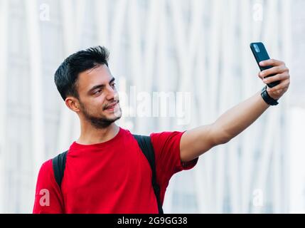 Junge Erwachsene Studenten, die ein Selfie mit einem Mobiltelefon vor einem unbestimmten urbanen Hintergrund machen Stockfoto