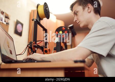 Niedriger Winkel des konzentrierten jungen Mannes, der 3D-Modell auf dem Laptop durchstöbert, bevor er am Tisch sitzt und im Studio arbeitet Stockfoto