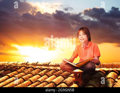 Junge sitzen auf einem Dach und lesen Buch, Blick auf den Sonnenuntergang Stockfoto