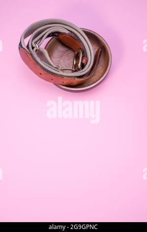 Vertikale Aufnahme eines abgerundeten Ledergürtels auf ästhetischem rosa Hintergrund mit Kopierfläche darunter. Stockfoto