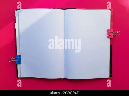 Leeres Notizbuch auf rotem Hintergrund. Leere Seiten eines offenen Buches, Platz für Schrift und Text. Blick von oben. Platz zum Kopieren, flach liegend. Stockfoto