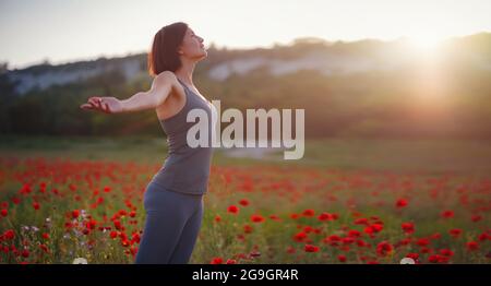 Junge schöne Frau mit erhobenen Armen im Frühjahr Mohnfeld. Sanfte Farben. Nachdenkliche, entspannte Atmosphäre. Stockfoto