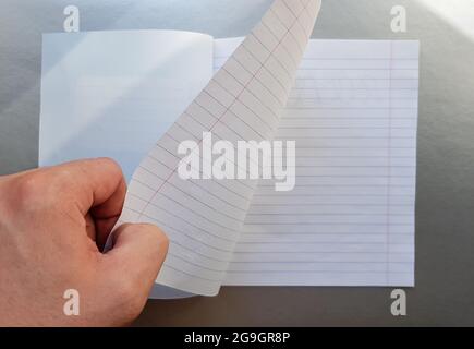 Designkonzept - Draufsicht einer hochwertigen männlichen Hand, die durch ein Blatt blau gestreiftes Notizbuch blättert. Draufsicht, Kopierbereich, flach liegend. Stockfoto