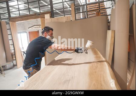 Mann in Atemschutzmaske Malerei Holzbretter in der Werkstatt. Handwerker moderne Möbel Fabrik malen Stockfoto