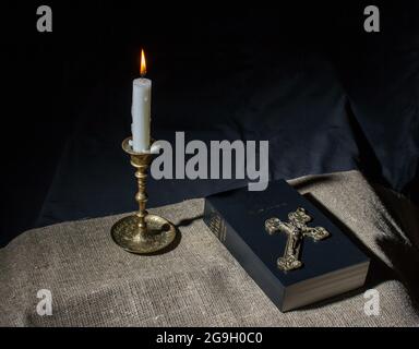 Bronzekreuz, brennende Kerze und bibel auf dem Tisch in der Nähe Stockfoto