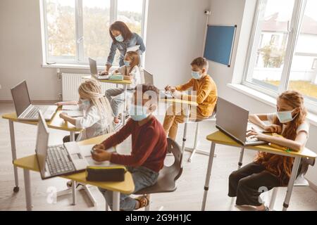 Kinder, die Masken tragen, sitzen im Unterricht an ihrem Schreibtisch Stockfoto