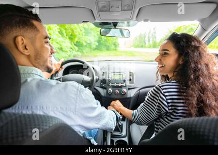 Rückansicht eines liebenden multirassischen Paares, das die Hände hält und sich lächelt, während es im komfortablen Auto sitzt. Glücklicher araber, der mit dem Auto unterwegs war Stockfoto