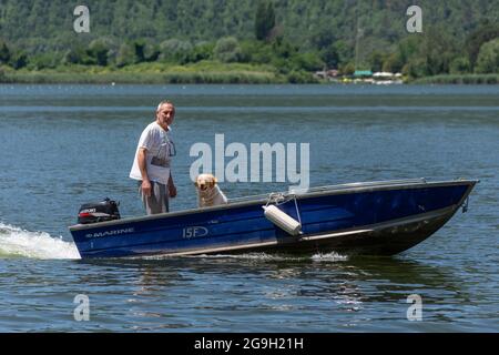 Ein Mann und sein Hund auf einem Boot, das den See von Piediluco pflügt, nach einer Angelzeit, Umbrien, Italien. Stockfoto