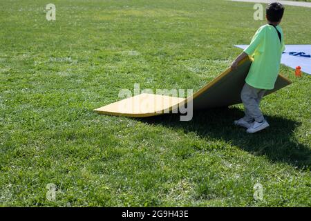 Der Mann trägt Sportkleidung. Matten für den Sport. Analyse des Sportgrunds. Nach dem Wettbewerb. Matten von der Straße putzen. Stockfoto