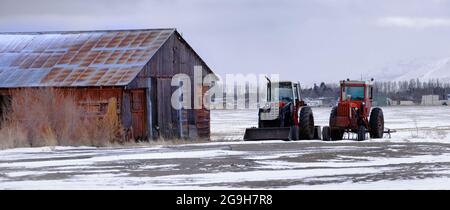 Traktoren auf einem Bauernhof in der Nähe eines alten Stallgebäudes Landwirtschaft Ausrüstung Stockfoto