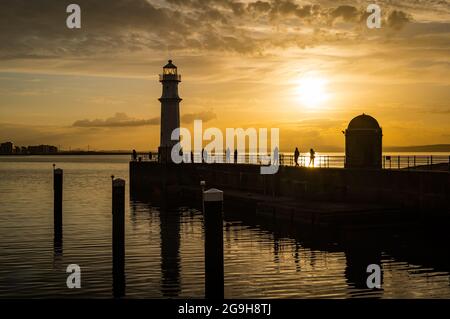 Am Pier am Hafen von Newhaven und am Leuchtturm wurde bei Sonnenuntergang in einem farbenprächtigen, orangefarbenen Himmel die Silhouette der Menschen dargestellt, Edinburgh, Schottland, Großbritannien Stockfoto