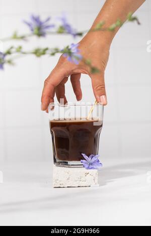 Chicorée Drink in einem transparenten Becher mit Chicorée Blumen im Vordergrund. Stockfoto