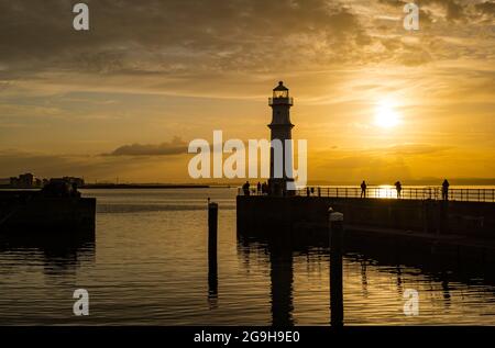 Am Pier am Hafen von Newhaven und am Leuchtturm wurde bei Sonnenuntergang in einem farbenprächtigen, orangefarbenen Himmel die Silhouette der Menschen dargestellt, Edinburgh, Schottland, Großbritannien Stockfoto