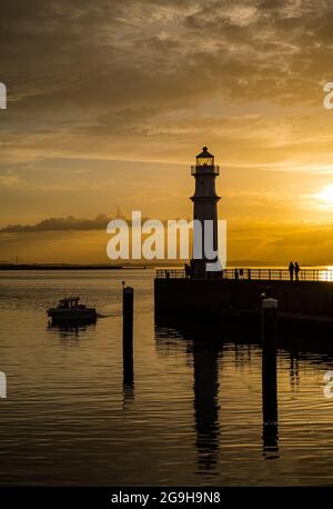 Am Pier am Hafen von Newhaven und am Leuchtturm wurde bei Sonnenuntergang in einem farbenprächtigen, orangefarbenen Himmel die Silhouette der Menschen dargestellt, Edinburgh, Schottland, Großbritannien Stockfoto