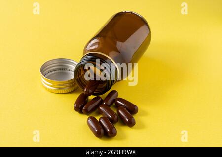 Medizinische Pillen oder Tabletten, die aus einer Medikamentenflasche auf gelbem Hintergrund auslaufen Stockfoto