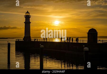 Am Pier am Hafen von Newhaven und am Leuchtturm wurde bei Sonnenuntergang in einem farbenprächtigen, orangefarbenen Himmel die Silhouette der Menschen dargestellt, Edinburgh, Schottland, Großbritannien Stockfoto