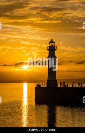 Am Pier am Hafen von Newhaven und am Leuchtturm wurde bei Sonnenuntergang in einem farbenprächtigen, orangefarbenen Himmel die Silhouette der Menschen dargestellt, Edinburgh, Schottland, Großbritannien Stockfoto