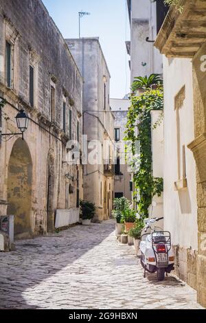 Otranto, Italien - 6. September 2017: Schöne enge typische Gassen der Altstadt in Otranto, Italien, Apulien. Weißer Roller auf der Straße geparkt. Keine Menschen, sonniger Tag. Stockfoto