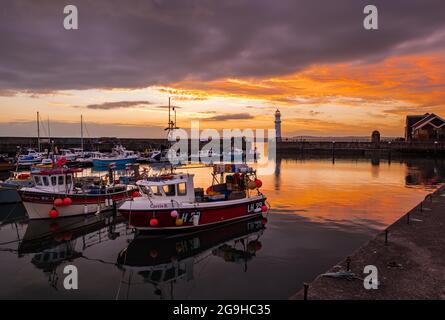 Kleine bunte Fischerboote, die bei Sonnenuntergang im Hafen von Newhaven mit Leuchtturm, Edinburgh, Schottland, Großbritannien, festgemacht sind Stockfoto