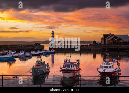 Kleine bunte Fischerboote, die bei Sonnenuntergang im Hafen von Newhaven mit Leuchtturm, Edinburgh, Schottland, Großbritannien, festgemacht sind Stockfoto