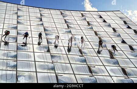 Hamburg, 22. Juli 2021: Fensterputzer hängen an Seilen an der façade der Elbphilharmonie und reinigen die riesige Glasfront des Großmodus Stockfoto