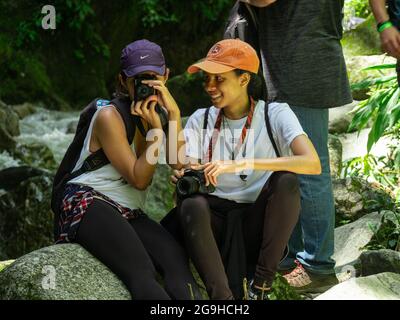 Amada, Antioquia, Kolumbien - Juli 18 2021: Hispanische Frauen sitzen auf Felsen am Flussufer und machen Fotos mitten in der Natur Stockfoto