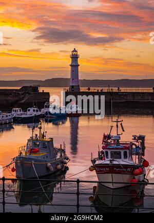 Kleine bunte Fischerboote, die bei Sonnenuntergang im Hafen von Newhaven mit Leuchtturm, Edinburgh, Schottland, Großbritannien, festgemacht sind Stockfoto