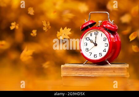 Rote Uhr auf Büchern mit Blättern. Zurück zur Schule im Herbst, Sommerzeit Hintergrund. Stockfoto