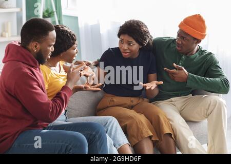 Zwei wütende, tausendjährige schwarze Freundinnen kämpfen, während sie sich zu Hause doppelt treffen, afroamerikanische Jungs umarmen sie und sitzen auf der Couch alle zusammen Stockfoto