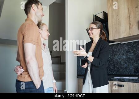 Seitenansicht Porträt eines jungen Paares im Gespräch mit einem Immobilienmakler während einer Tour durch die Wohnung Stockfoto