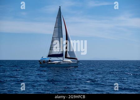 Segeln in der Ägäis Griechenland. Segelboot mit offenen weißen Segeln, ruhigem, gewellten Meer, blauer Himmel im Hintergrund, sonniger Tag. Ferien Cyclades i im Sommer Stockfoto