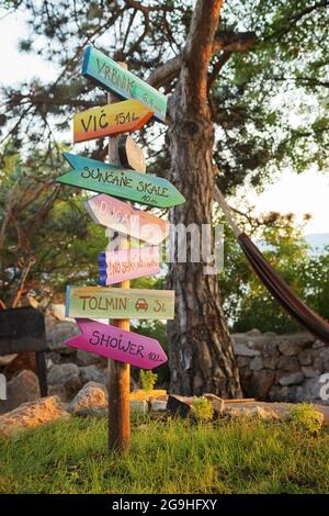 Farbenfrohe und amüsante Wegweiser mit Entfernungen zu verschiedenen Orten und Städten unter Kiefern mit Hängematte im Lager an der kroatischen Küste Stockfoto