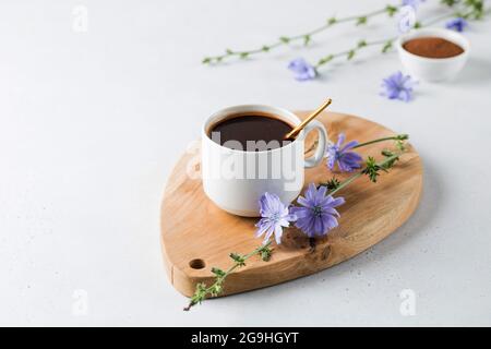 Chicorée Drink in einem weißen Becher mit Chicorée Blumen daneben auf einem Holzbrett. Stockfoto