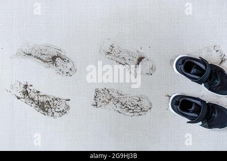 Schmutzige Schuhe, die schlammige Fußabdrücke auf dem Teppich hinterlassen. Hochwertige Fotos Stockfoto