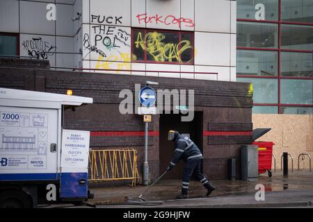 Bristol, Großbritannien. März 2021. Am Morgen, nachdem Bristol die schlimmste Straßengewalt seit mehreren Jahren erlebt hat, beginnt der Reinigungsprozess mit dem Schrubben von Graffiti und dem Aufräumen von Trümmern. Die Demonstranten griffen gestern die Polizei an, nachdem Tausende von Menschen an einem Protest teilgenommen hatten, den die Beamten „nachdrücklich empfohlen“ hatten, nicht daran zu teilnehmen. Die Polizisten erlitten Knochenbrüche und Polizeifahrzeuge wurden angezündet, als sich wütende Szenen im Stadtzentrum von Bristol abspielten. Im Bild: Ein Arbeiter fegt Entwbris vor der Bridewell Polizeistation, wo die Aufmerksamkeit der Randalierer gestern Abend konzentriert wurde. Stockfoto