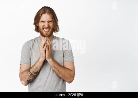 Schlauer blonder Kerl, der wie böses Genie schielt, stählerner Finger nachdenklich, hat eine interessante Idee, Plan vorbereiten, etwas schemeln, Über Weiß stehend Stockfoto