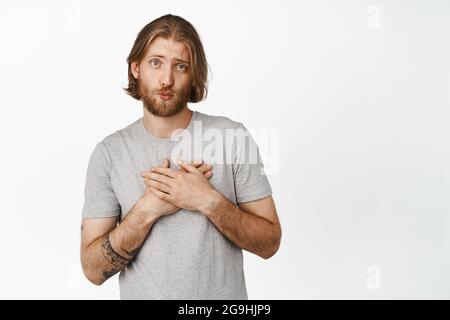 Niedlich und dumm blonde bärtige Kerl Pucker Lippen, küssen Gesicht, Hände auf Herz, zeigt schüchtern zarten Ausdruck, geschmeichelt, berührt Stockfoto